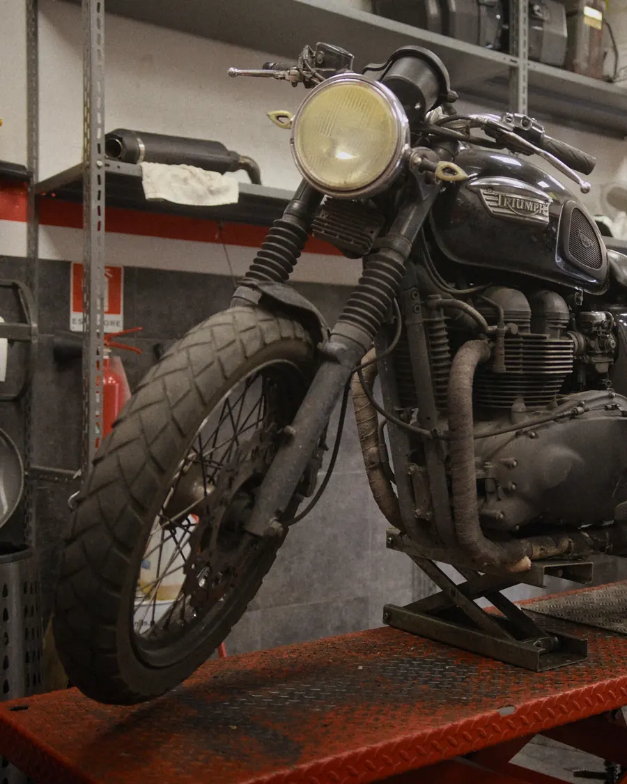 Una Triumph nera sul ponte rosso, davanti agli scaffali dell'officina